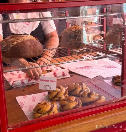 Cinnamon Pompe pastries and country loaves in a red-framed display case at Pompe, a Marseille boulangerie.