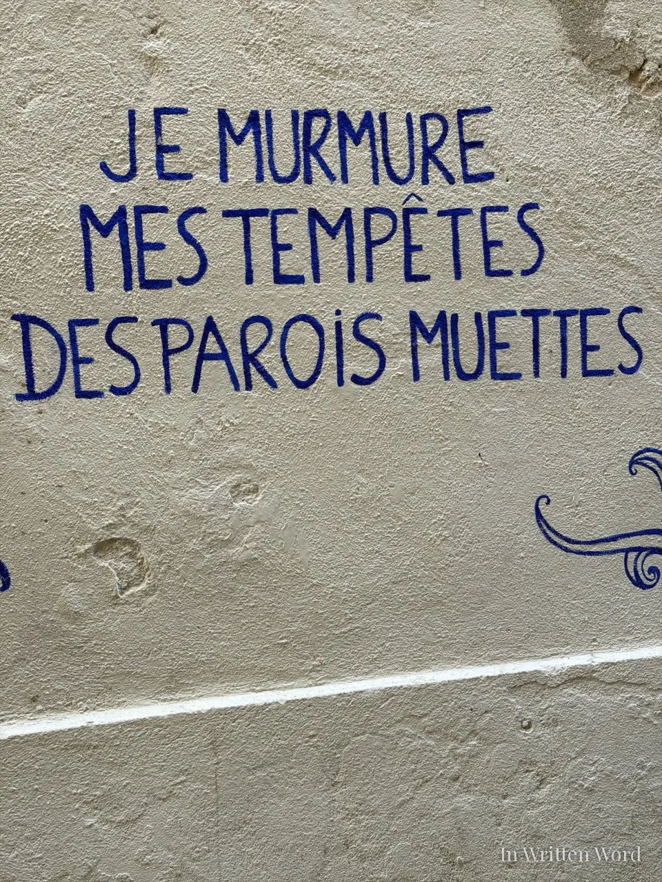 Hand-painted blue lettering on a textured cream wall in Marseille that reads "Je murmure mes tempêtes des parois muettes.