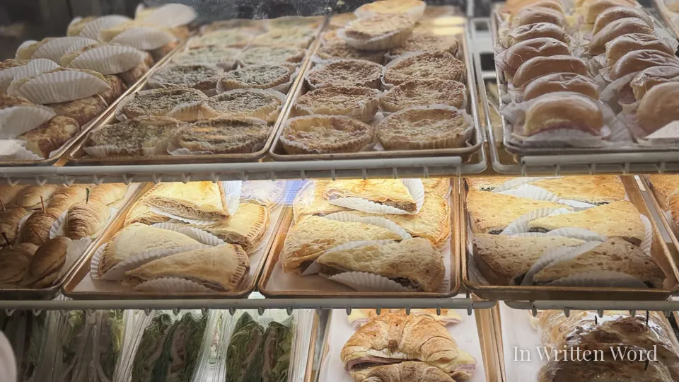 Display case at Versailles Restaurant in Miami filled with Cuban pastries, including pastelitos, croquettes, and sandwiches arranged on metal trays behind glass.