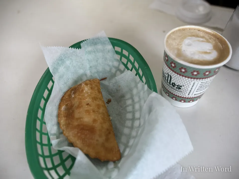 Green plastic basket holding a fried empanada beside a cup of café con leche at Versailles Restaurant in Miami.