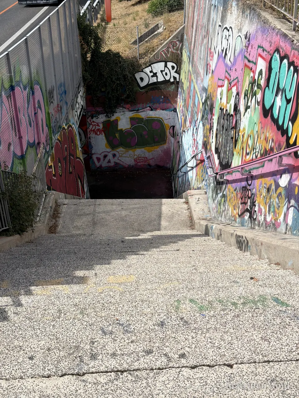A concrete staircase descending into an underpass, both walls covered in bright multicolored graffiti.