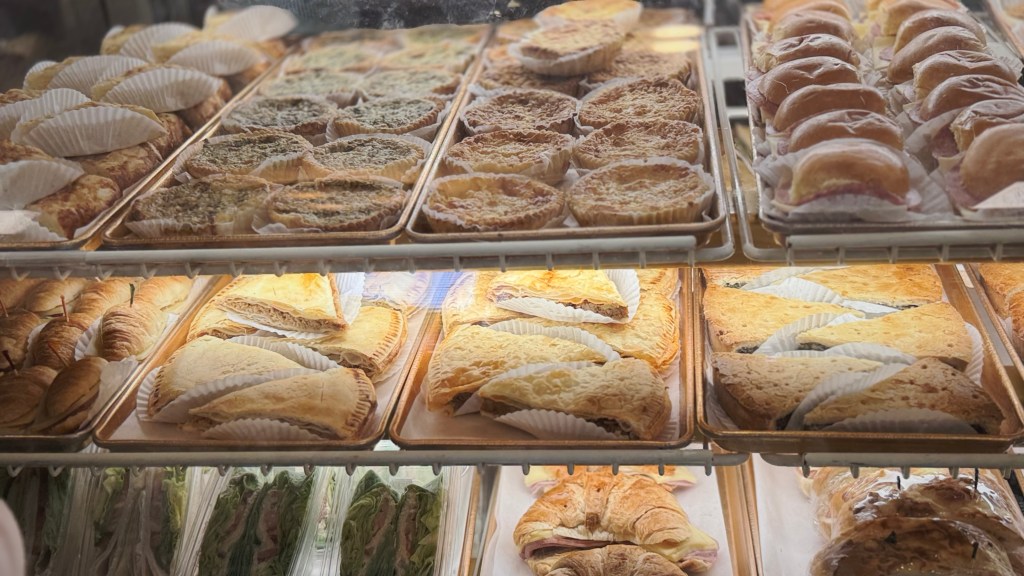 Display case at Versailles Restaurant in Miami filled with Cuban pastries, including pastelitos, croquettes, and sandwiches arranged on metal trays behind glass.