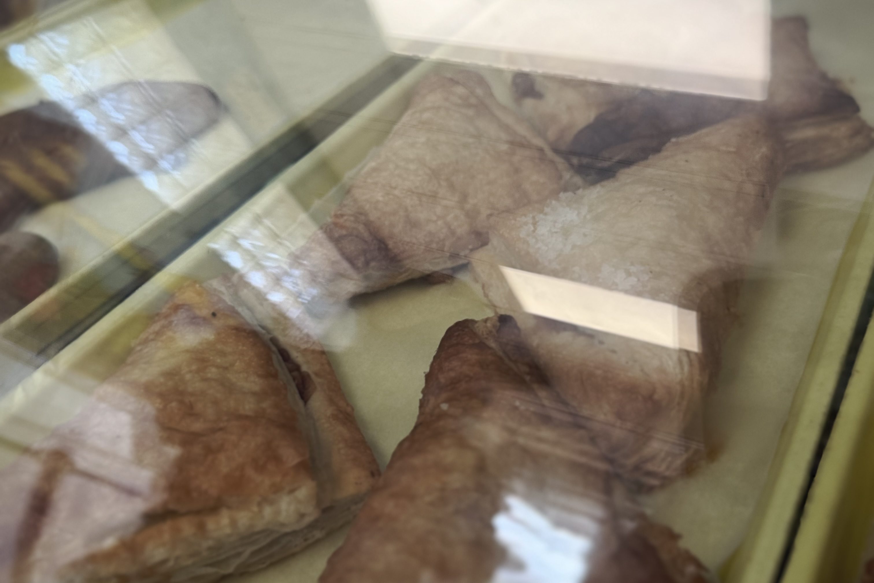 Pastries displayed behind glass at Piman Bouk Bakery in Little Haiti, Miami, including triangular puff pastries arranged on trays.