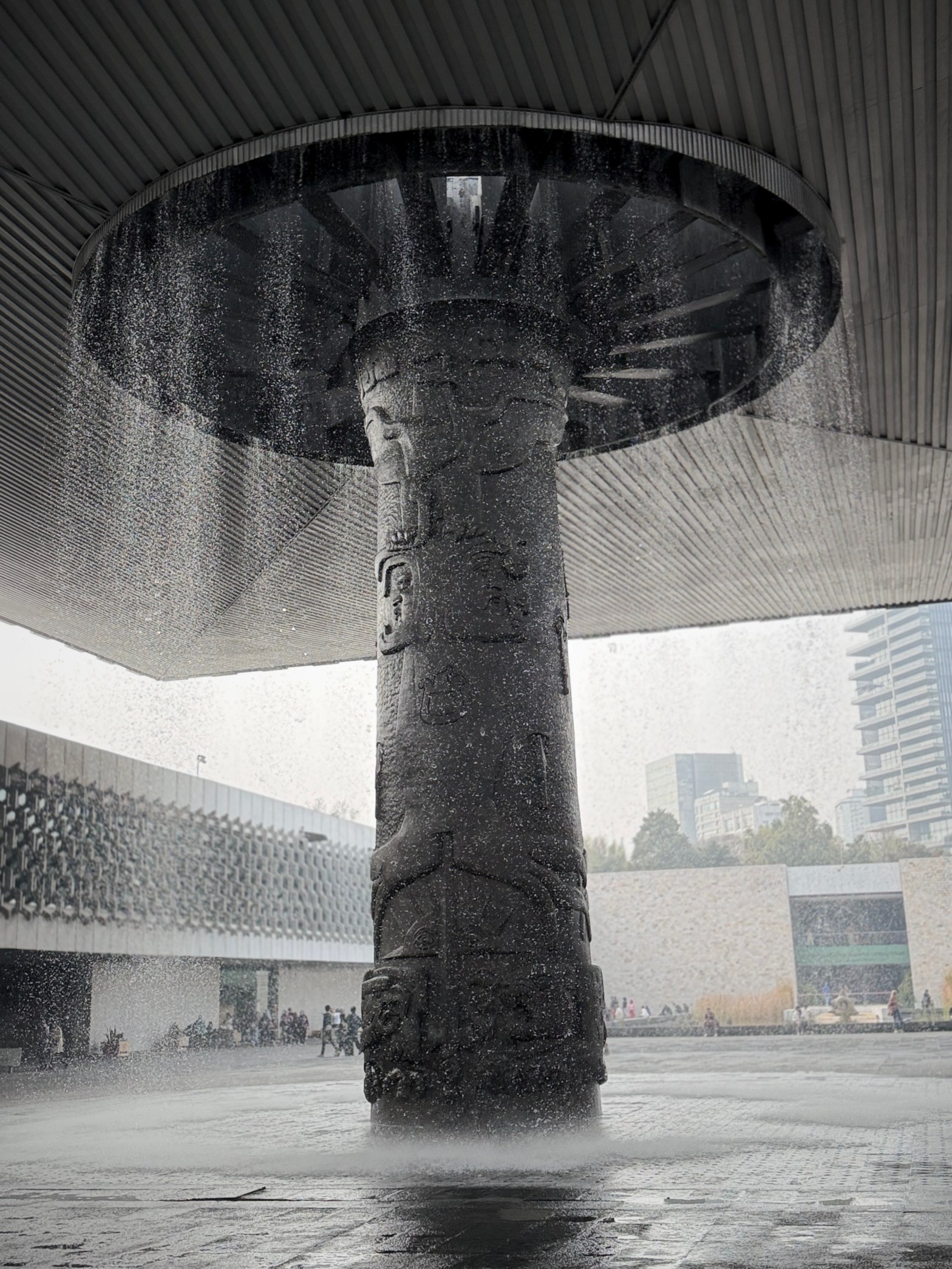 Floating concrete canopy fountain at Museo Nacional de Antropología in Mexico City, water cascading over a carved stone column in the central courtyard.